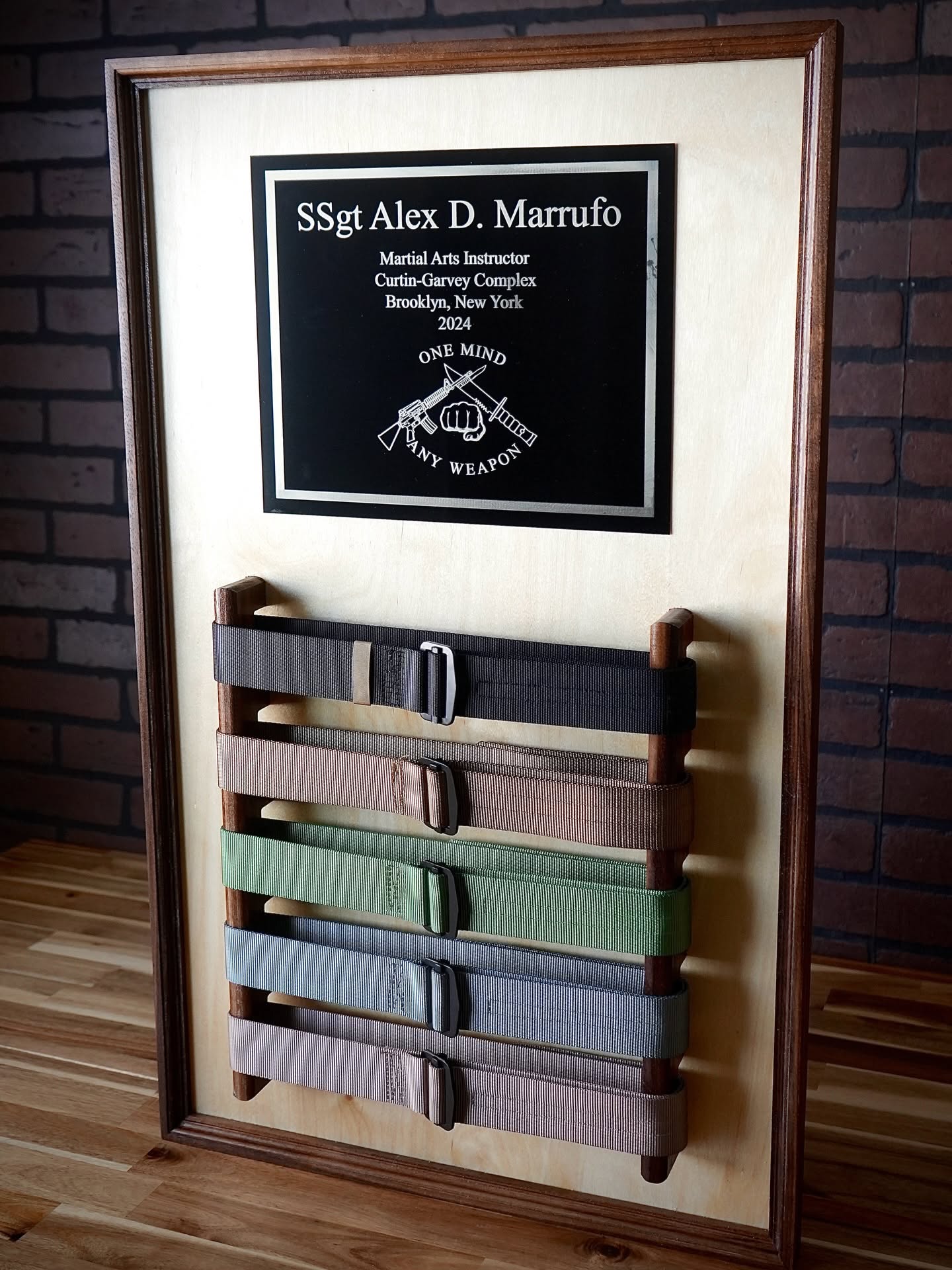 Personalized martial arts belt display photographed on a wood tabletop against a brick wall