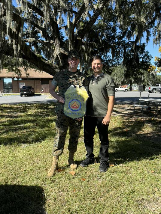 Two customers holding a badge-shaped COMMSTRAT plaque