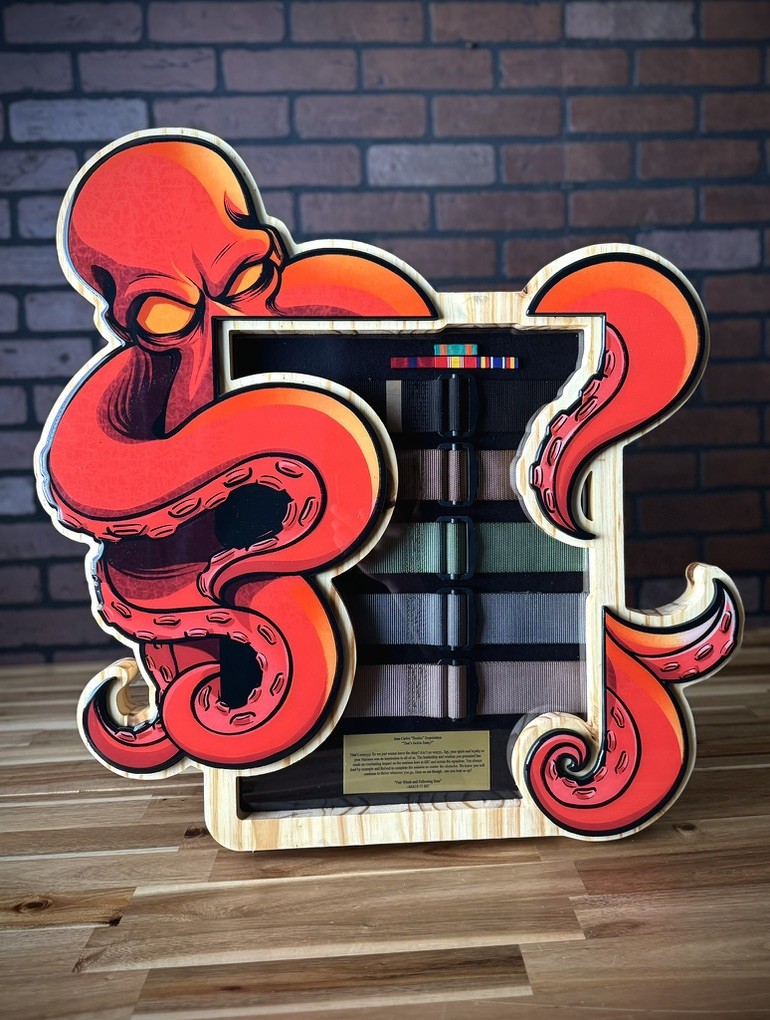 Custom red octopus shadow box with martial arts belts, ribbons, and a personalized message, against a brick wall