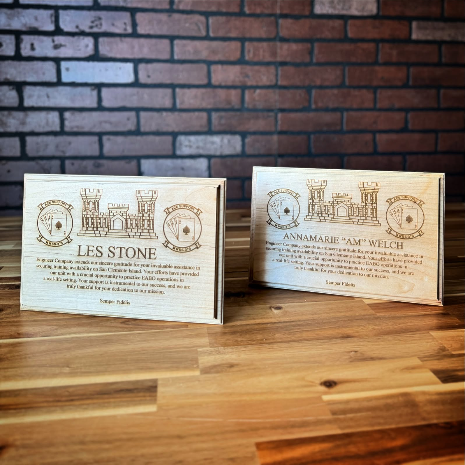 Two personalized engraved wooden plaques displayed against a brick wall