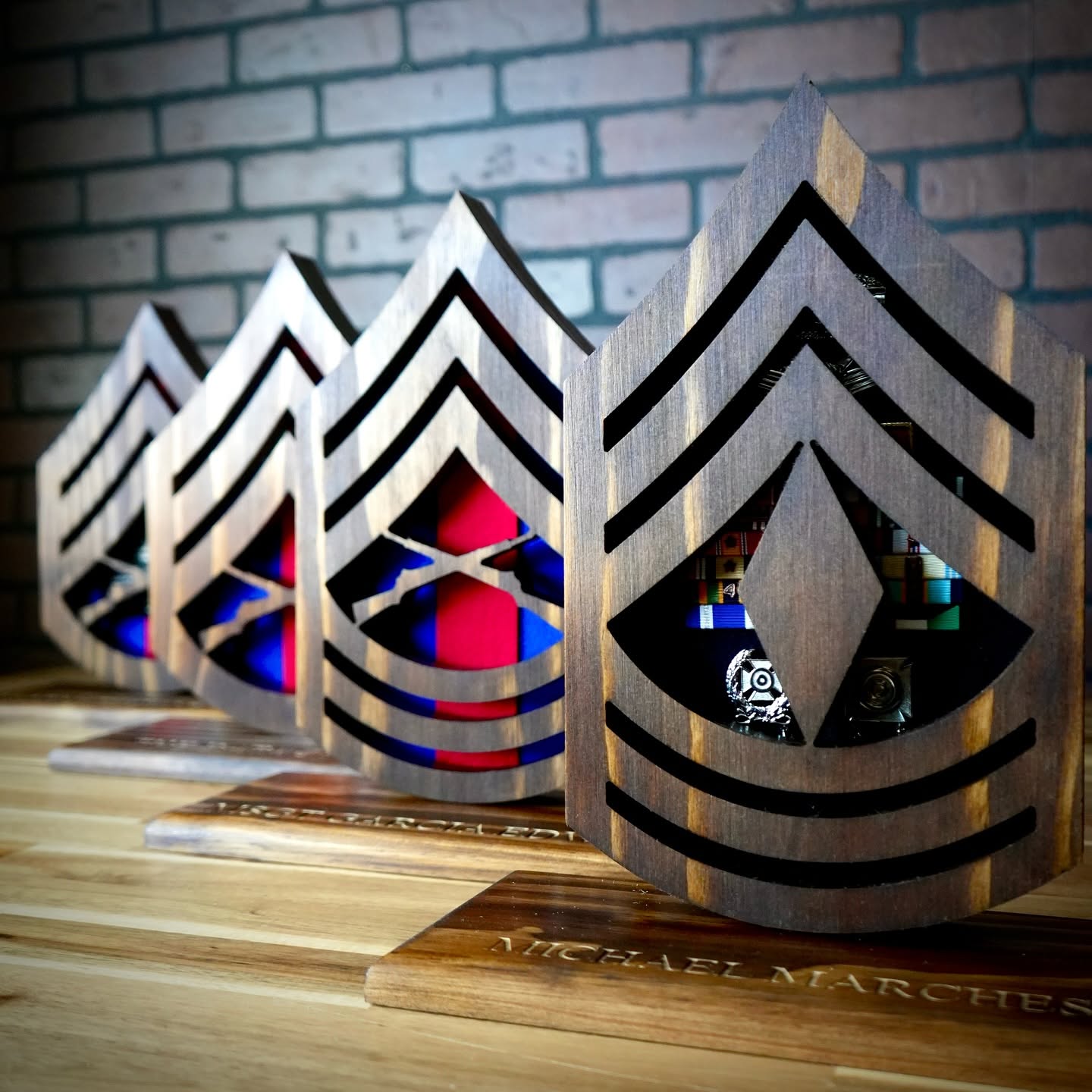 Four wooden military rank desk cases lined up on a tabletop against a brick wall