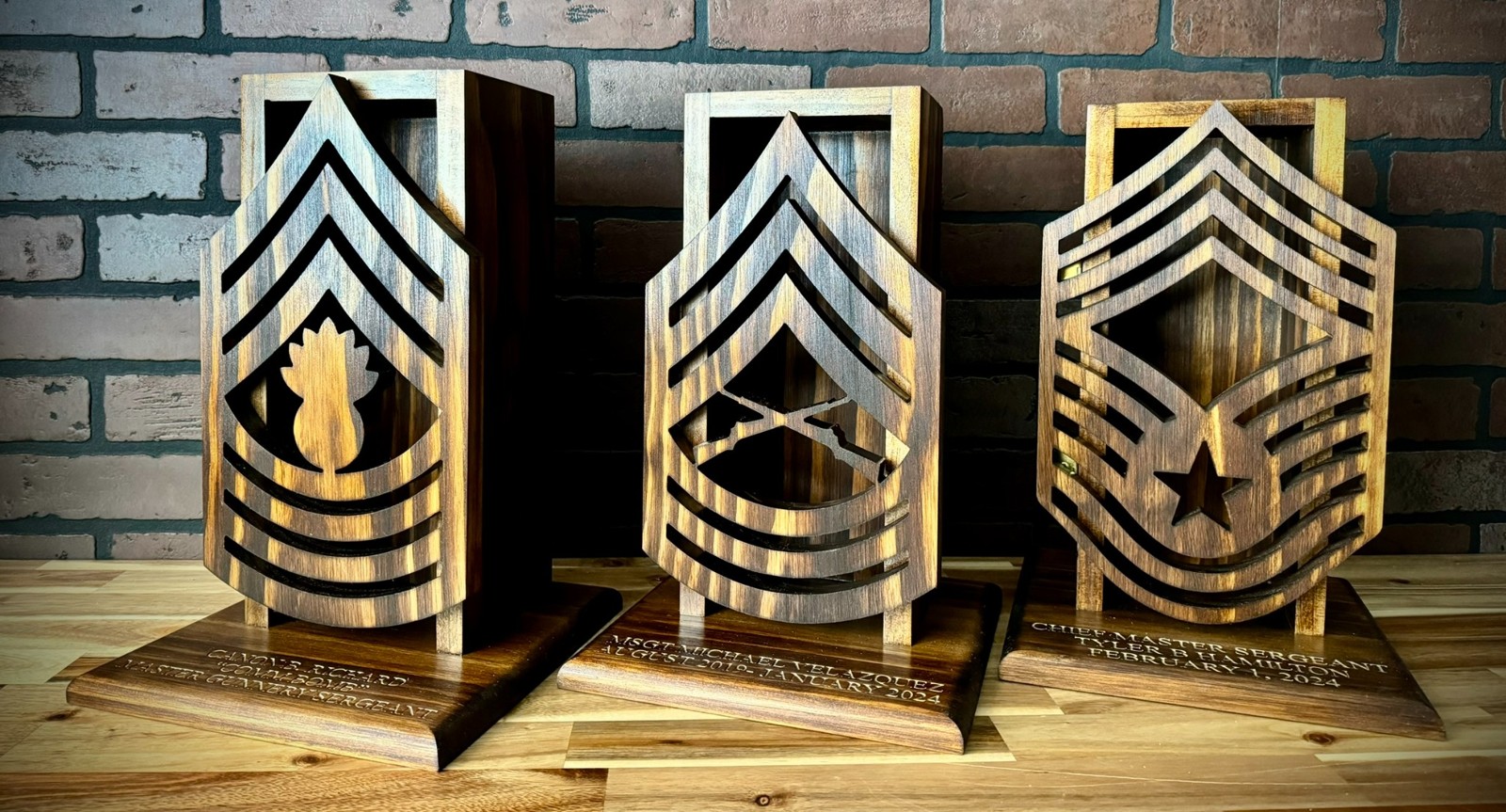 Three custom wooden military rank whiskey cases displayed together against a brick wall